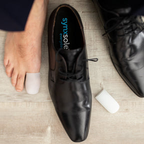 man with foot next to work shoe big toe wearing synxgeli large toe sleeve, ideal for treating, reducing or preventing corns, blisters and toe deformities