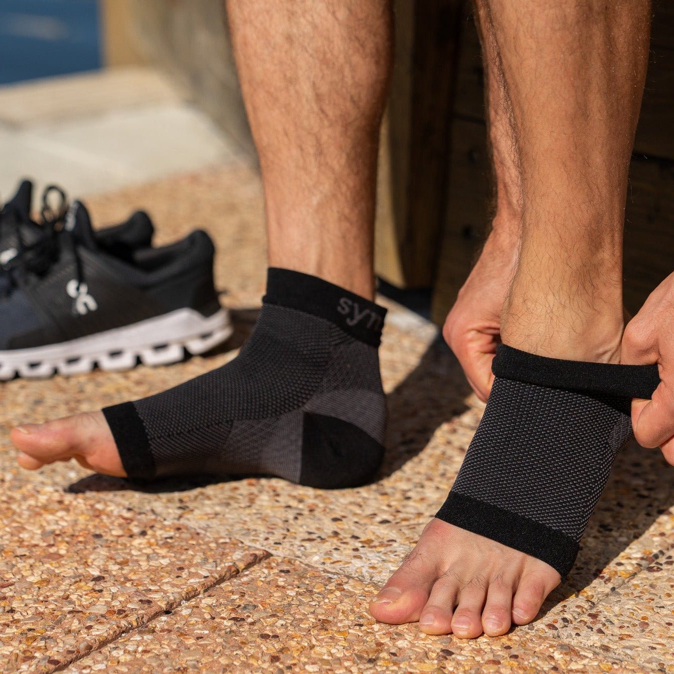 a man placing a pair of synxplus foot and ankle compression sleeve on his foot to assist relieve pain, swelling, inflammation