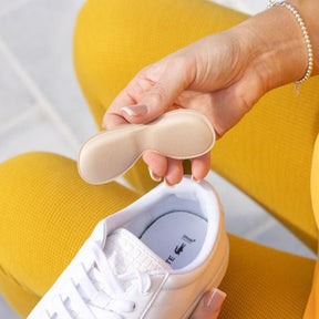 a lady holding a synxgeli heel grip about to place in her white sneaker to prevent rubbing on the heel