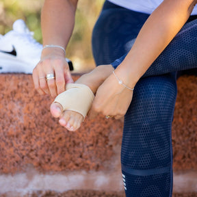 lady pulling on a synxgeli bunion sleeve to treat bunions and bony prominences by protecting and relieving soft tissue and the big toe joint from unwanted stress