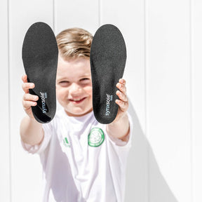 young boy in soccer outfit holding up pair of synxsole kids insoles, severs disease, growing pains
