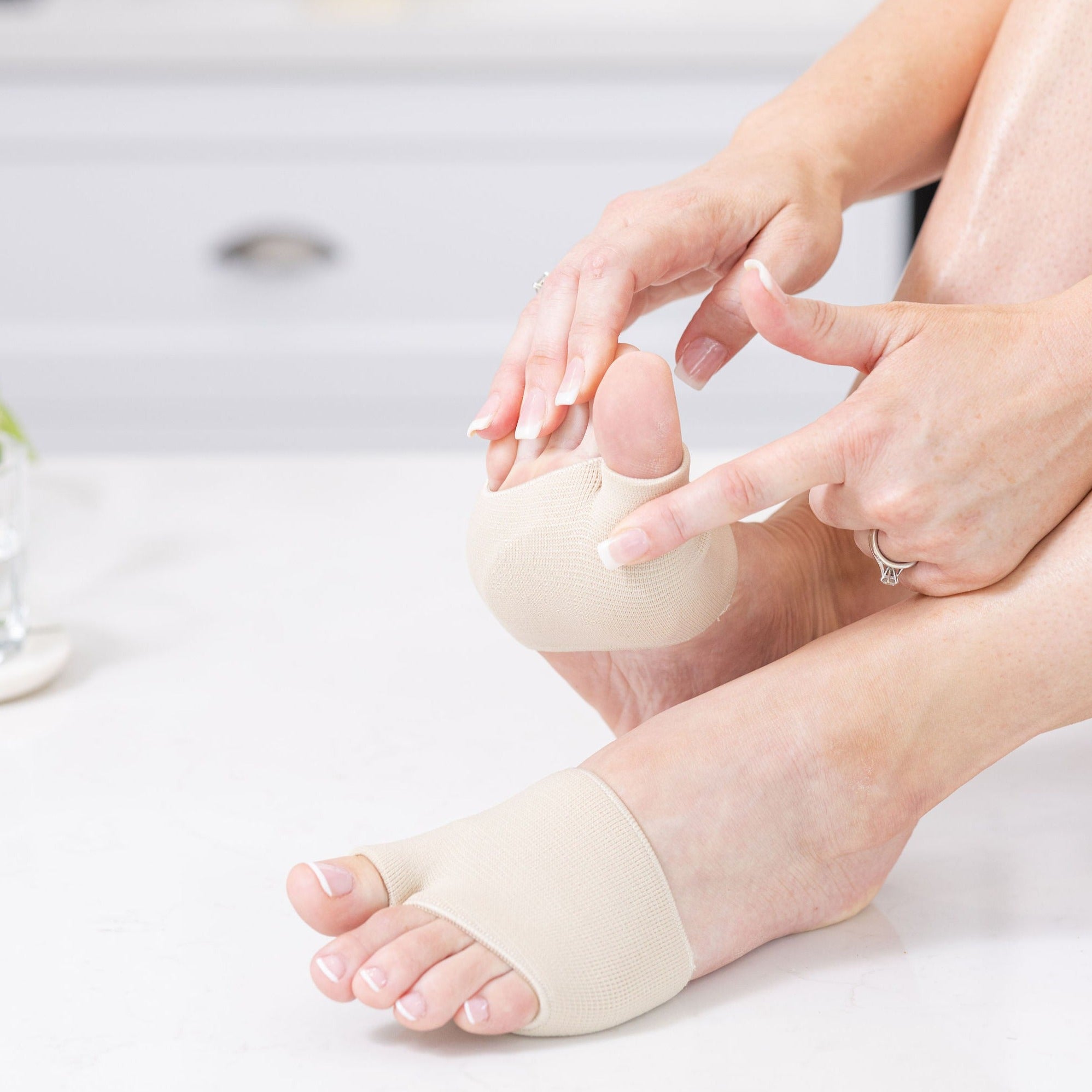 lady pointing to ball of foot area wearing a pair synxgeli forefoot cushions to demonstrate cushioning to treat blisters, neuromas, corns, calluses and ball of foot pain