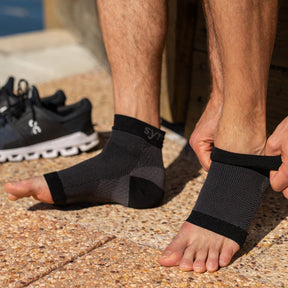 a man placing a pair of synxplus foot and ankle compression sleeve on his foot to assist relieve pain, swelling, inflammation