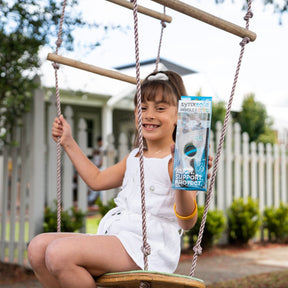 young girl on swing holding up packet of synxsole kids insoles, severs disease, growing pains