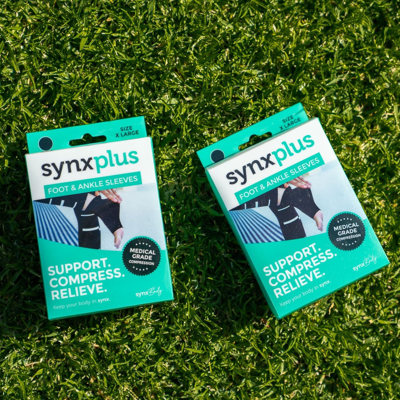 packets of synxplus foot and ankle compression sleeves to assist relieve pain, swelling, inflammation laying on the grass