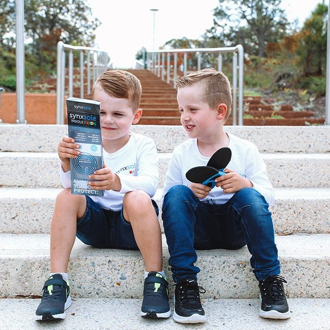 two young boys looking at synxsole kids insole packet sitting on steps, severs disease, growing pains