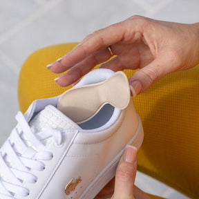 a lady placing a synxgeli heel grip on the back of her white sneaker to prevent rubbing on the heel