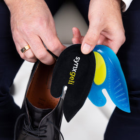 man holding synxgeli heel cushions next to work shoes, heel pain